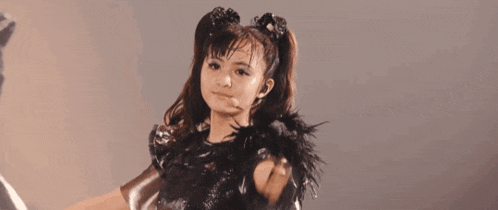 a young girl in a black dress with feathers on her shoulder is dancing on a stage .