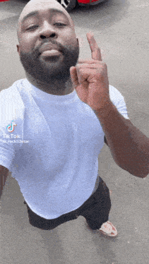 a man with a beard is giving the middle finger while wearing a white shirt .