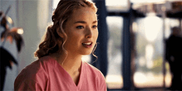 a woman in a pink scrub top is smiling in a hospital .