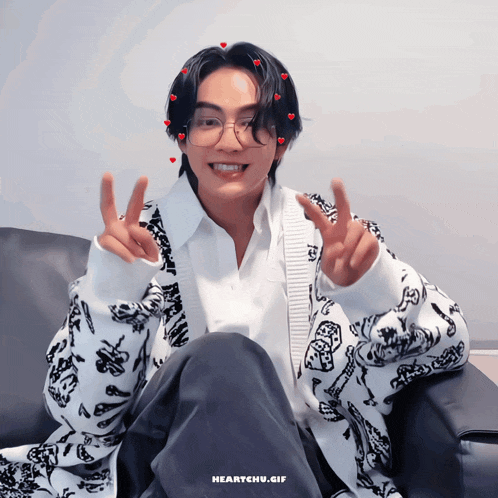 a man wearing glasses and a white shirt is sitting in a chair and giving a peace sign