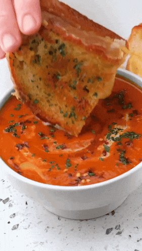 a person is dipping a piece of grilled cheese into a bowl of soup
