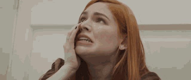 a woman with red hair and a ring on her finger is crying .