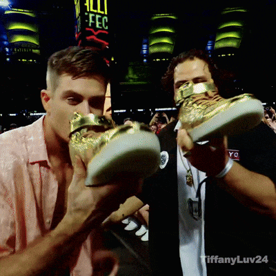 a man is holding a pair of shoes in front of a sign that says " all fc "