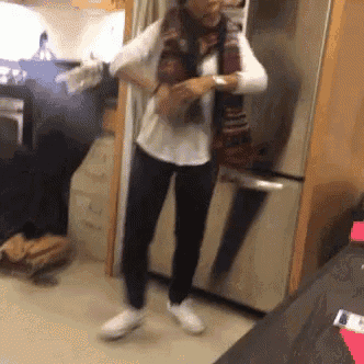 a woman wearing a scarf and a white shirt is standing in front of a refrigerator .