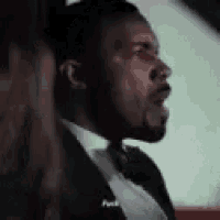 a man in a tuxedo and bow tie is sitting in a car with his mouth open .