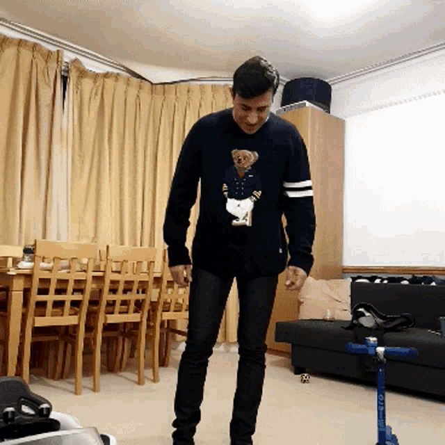 a man wearing a sweater with a teddy bear on it is standing in a living room