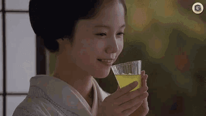 a woman in a kimono is holding a glass of green tea .