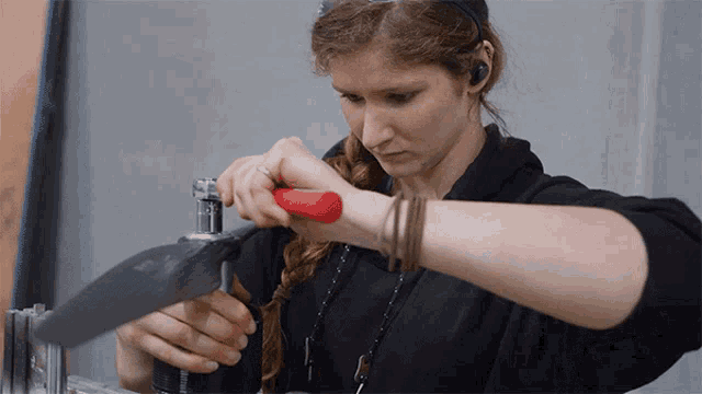 a woman in a black shirt is working on a piece of metal with a red handle