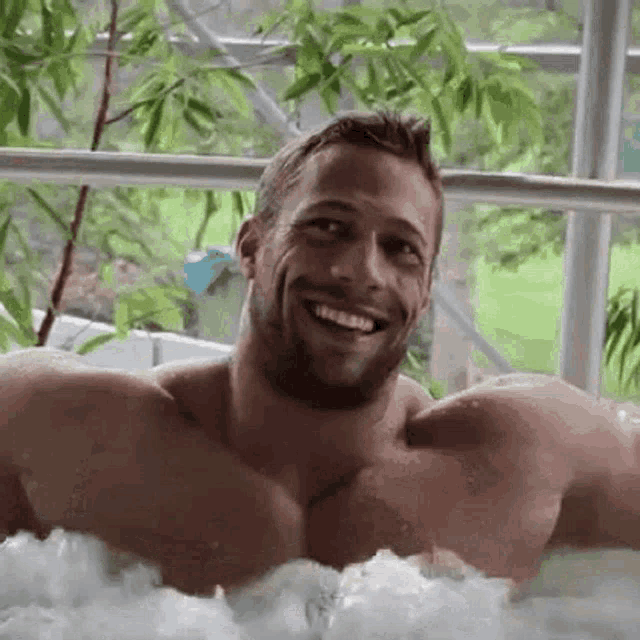 a shirtless man is smiling while taking a bath in a jacuzzi .