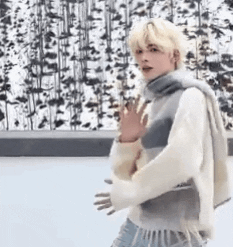 a young man in a sweater and scarf is standing on a ice rink .