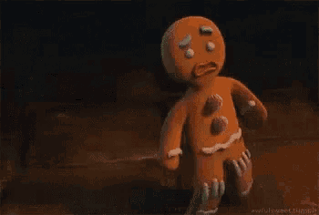 a gingerbread man is standing on a wooden floor in a dark room holding a lollipop .