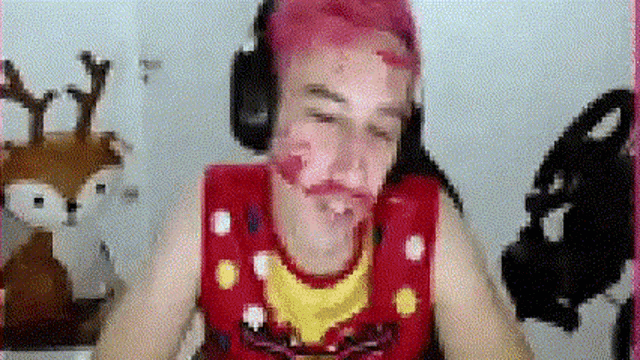 a man with pink hair is making a funny face while wearing headphones and a red vest .