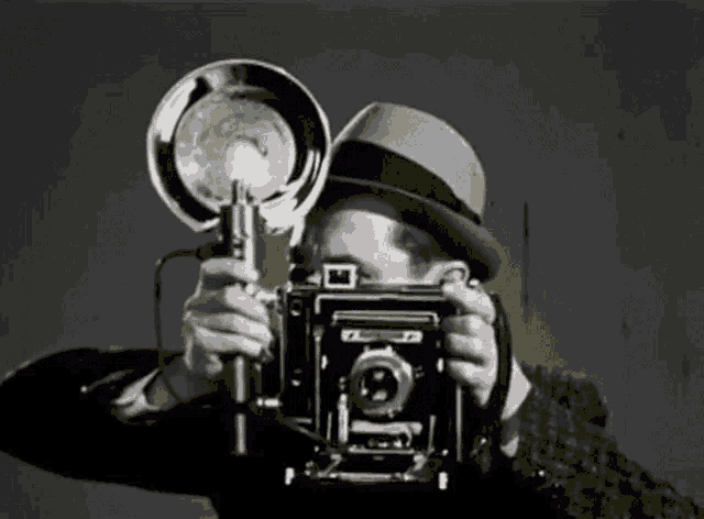 a man in a hat is taking a picture with an old camera .