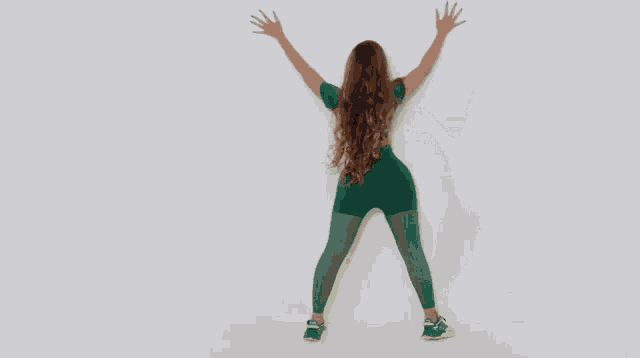 a woman in a green crop top and green leggings is dancing against a white background .