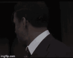 a man in a suit and tie is standing in front of a black background .