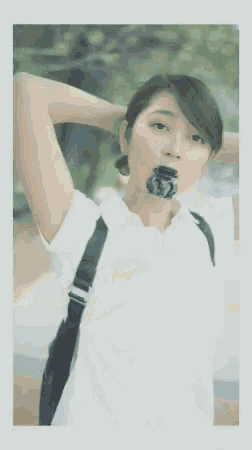 a woman in a white shirt is holding her hair in a ponytail and wearing a bandana .