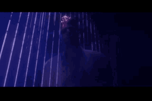 a man in a white shirt is standing in a dark room with purple lights coming from the ceiling .