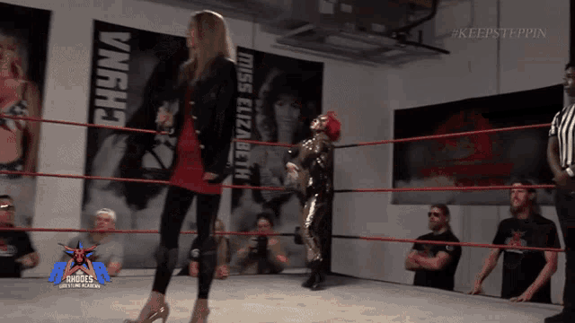 a woman in high heels stands in a wrestling ring with miss elizabeth posters behind her