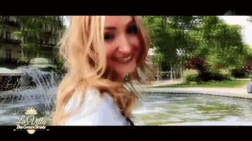 a woman is smiling in front of a fountain with la villa written on the bottom