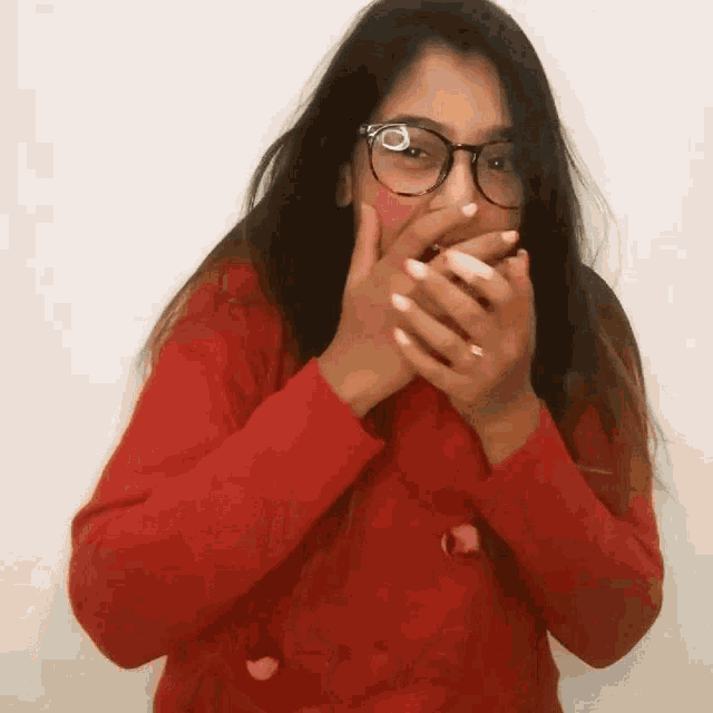 a woman wearing glasses and a red sweater covers her mouth with her hands