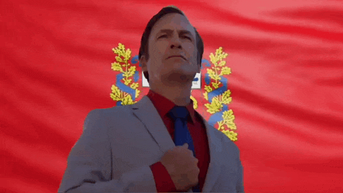 a man in a suit and tie stands in front of a flag