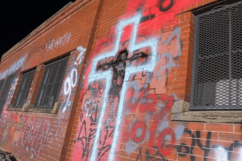 a brick wall with graffiti on it including a cross that says ' jesus ' on it