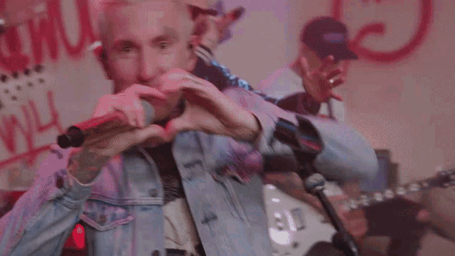 a man in a denim jacket is making a heart shape with his hands while singing into a microphone