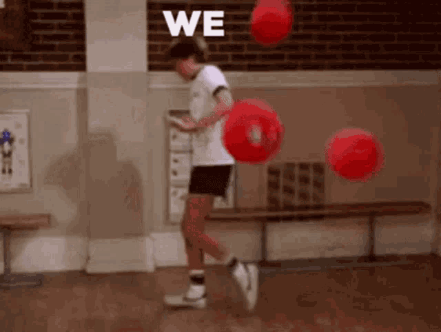a boy is playing with red balls in a gym and the word we is on the wall behind him .