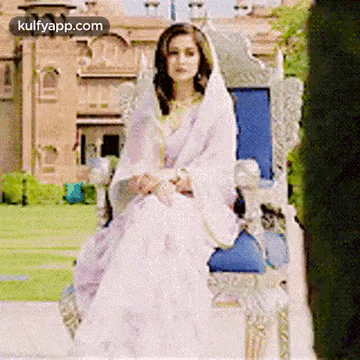 a woman in a white dress and veil is sitting on a throne .