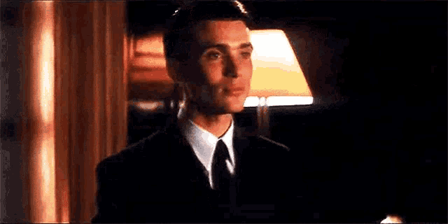 a man in a suit and tie is standing next to a lamp in a dark room .