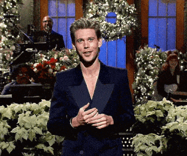 a man in a tuxedo is standing in front of a christmas tree and flowers .
