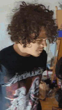 a man with curly hair is wearing a metallica t-shirt .