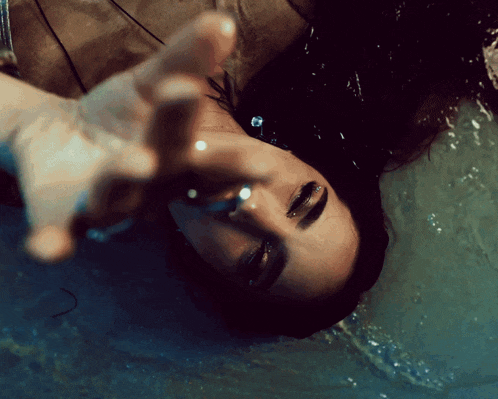 a woman is laying in the water and reaching out for something