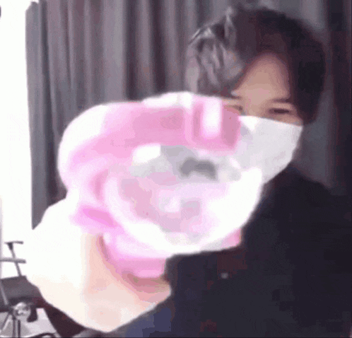a man wearing a face mask is holding a pink balloon in front of his face .