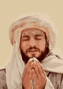 a man with a beard is praying with his eyes closed and his hands folded .
