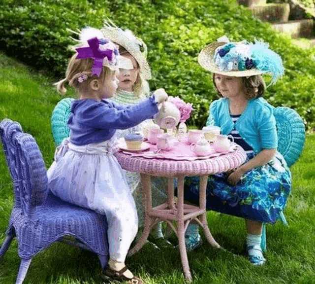 three little girls are sitting at a table playing with tea set .