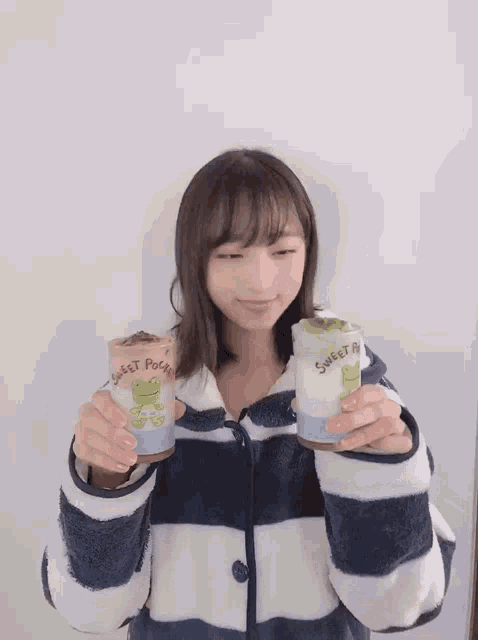 a girl in a striped jacket is holding two cups that say sweet pocket on them
