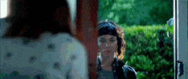a woman with short hair is standing in front of a door looking at another woman .
