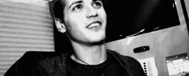 a black and white photo of a young man smiling while sitting in a chair .