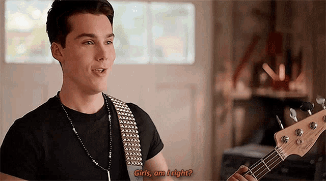 a young man is playing a bass guitar in a room and talking to someone .