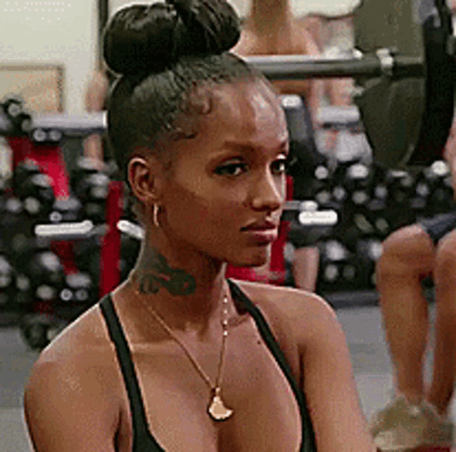a woman is sitting in a gym wearing a black tank top and a necklace .