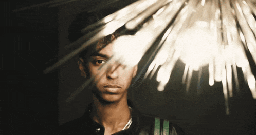 a man with a necklace around his neck looks at the camera with a light behind him