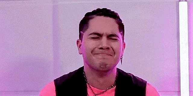 a man wearing a pink shirt and a black vest is making a face .