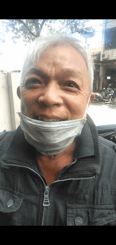 a man wearing a face mask and a black jacket smiles