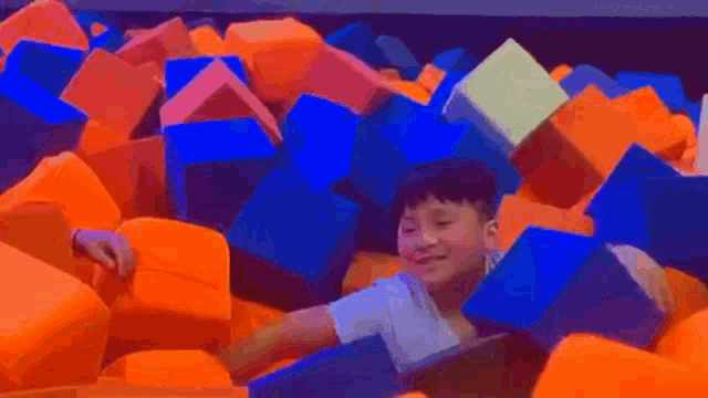 a young boy is laying in a pile of colorful foam cubes .