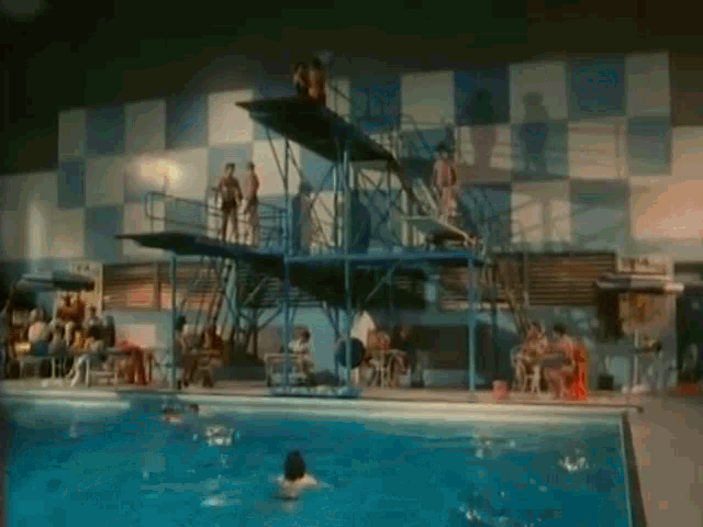a group of people are swimming in a swimming pool with a diving board .