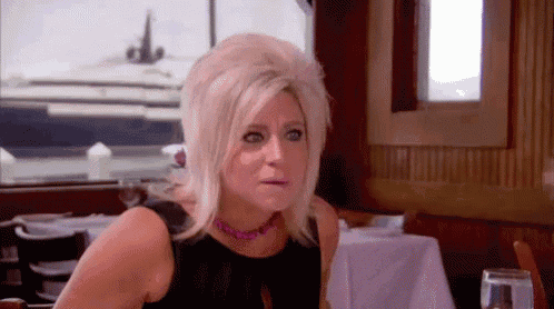 a woman is sitting at a table in a restaurant with a yacht in the background .