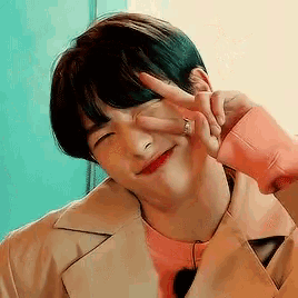 a young man wearing a trench coat and a pink shirt is making a peace sign