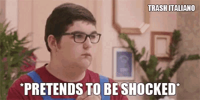 a young man wearing glasses and a red shirt is making a funny face and saying pretends to be shocked .
