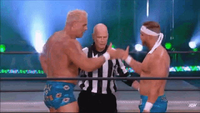 two men are wrestling in a ring while a referee watches .